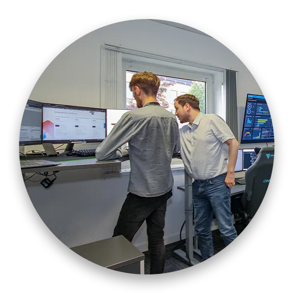 Two IT professionals collaborating at a standing desk with multiple monitors